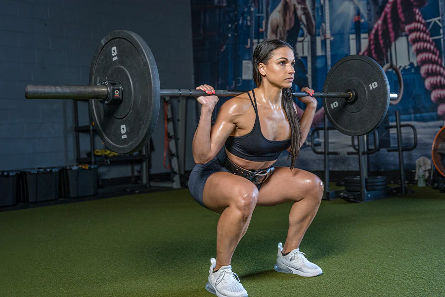 A Woman Engages In A Squat With A Barbell At The Gym